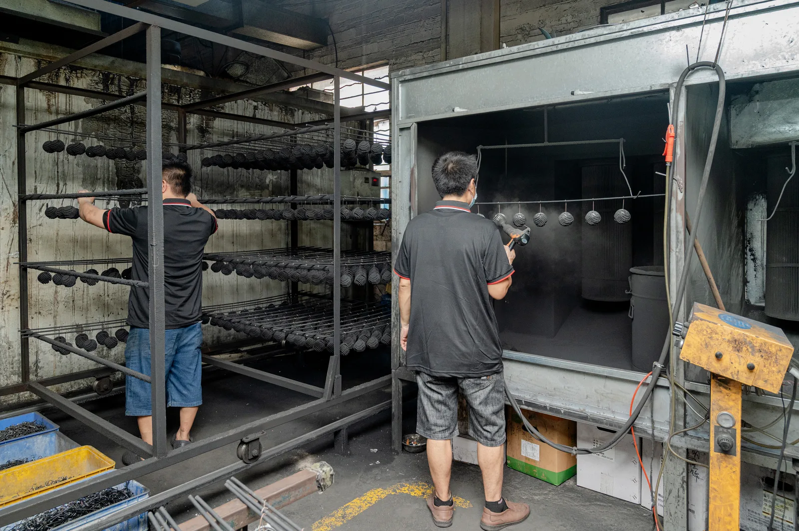 Spray coating workshop applying finish to metal light housings before assembly