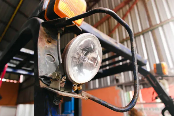 Close-up of a round headlight and orange marker light on a blue forklift frame.