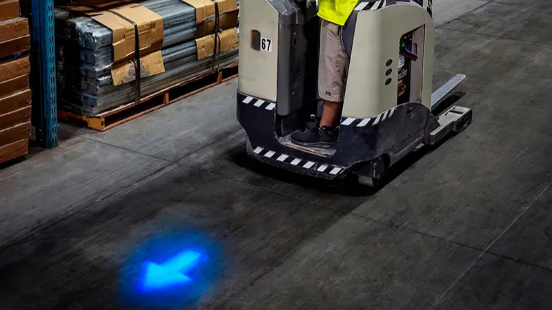 Forklift projecting a blue arrow safety light in a warehouse aisle to signal vehicle presence and direction