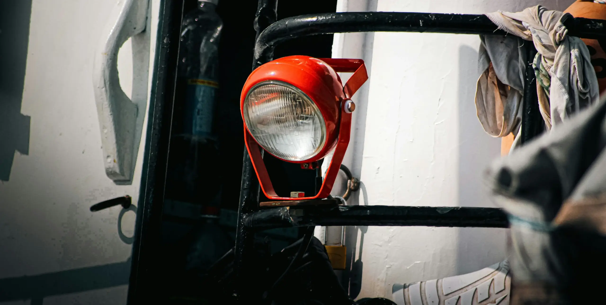 A bright red industrial work light mounted on a black metal frame, illuminated against a white wall with draped fabric nearby